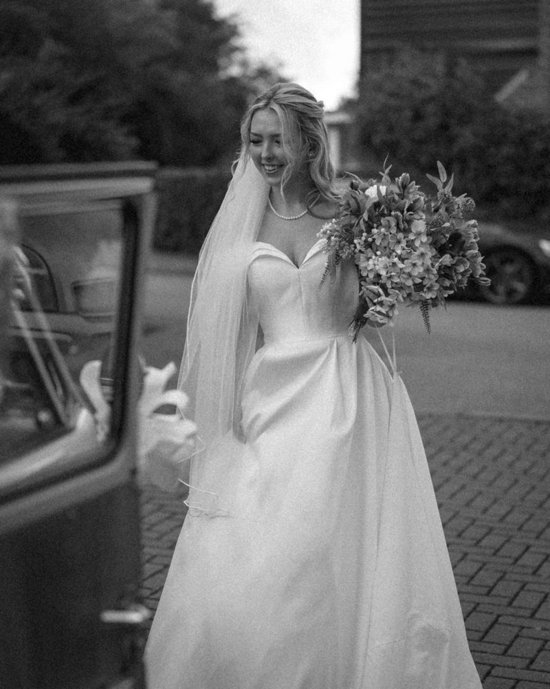 Black and white candid of bride beside vintage car