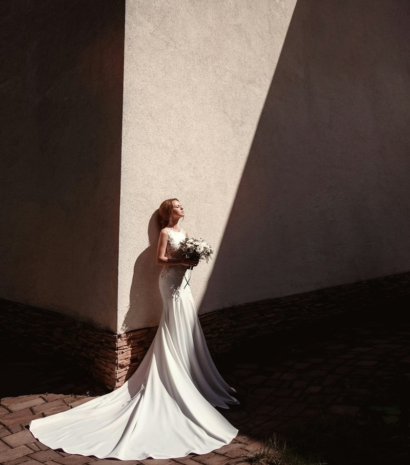 Bride in a flowing white gown standing in a beam of natural sunlight
