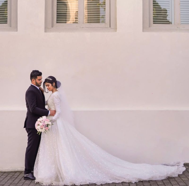 Bride with long train wedding dress against white wall
