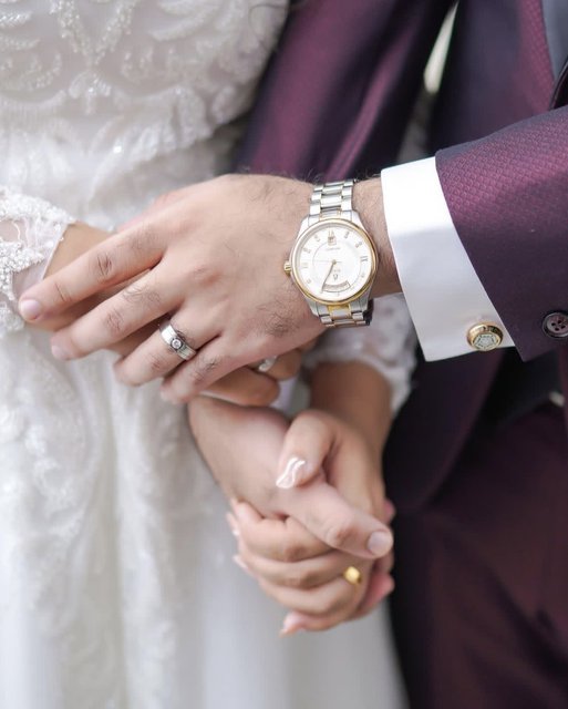 Bride and groom holding hands with wedding rings and watch detail
