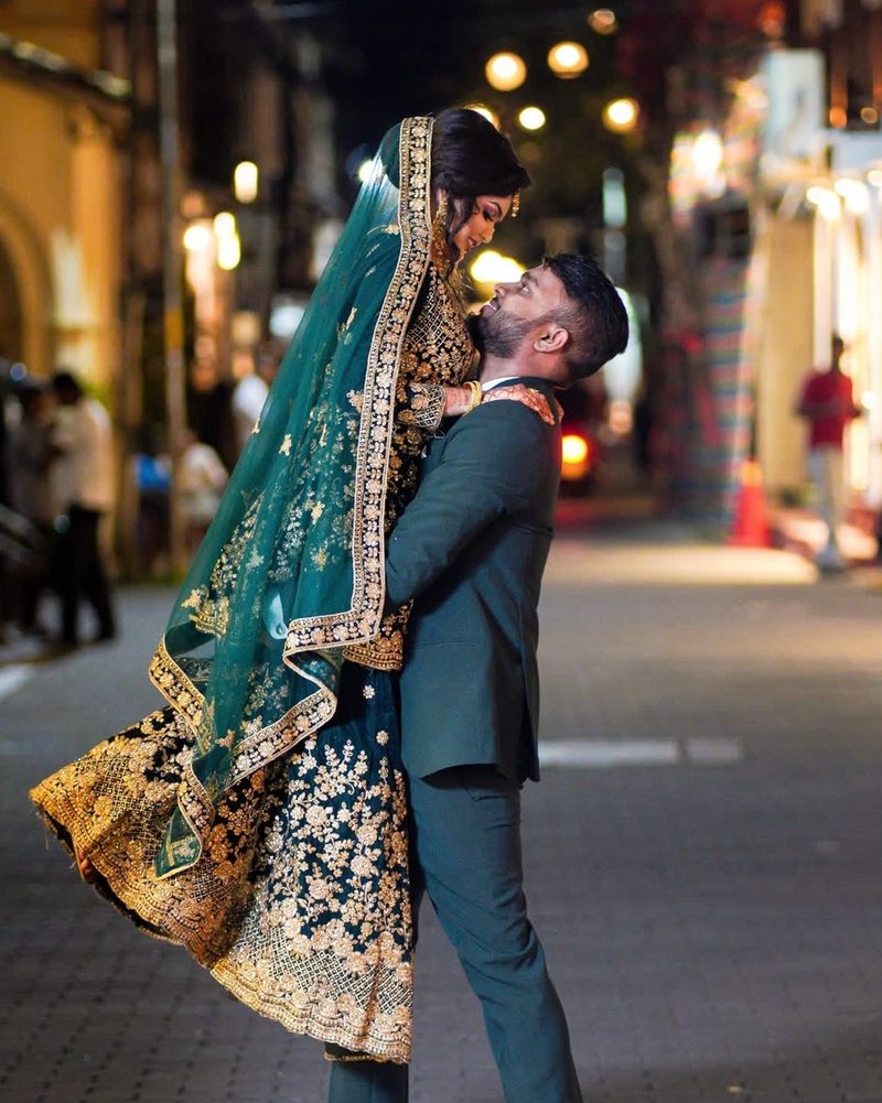 Groom lifting bride in flowing teal lehenga on a lit street