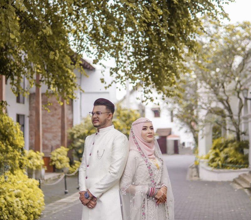 Couple in white attire under green tree canopy